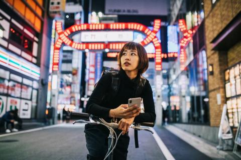 A woman on a bike with a neon-lit city background