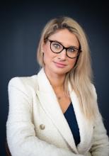 A blonde woman smiling at the camera wearing a white blazer