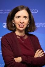 A woman with dark hair standing with arms crossed, smiling at the camera